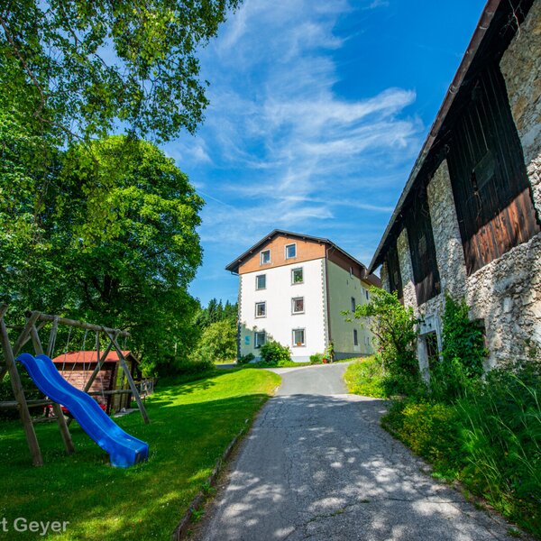 Außenansicht des Bauernhofs mit Kinderspielplatz auf der Rasenfläche und Zufahrt zum Hauptgebäude.