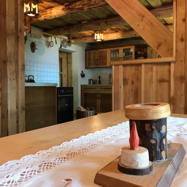 The farmhouse kitchen and dining area, featuring a wooden table with a lace runner, a fully equipped kitchen, and exposed wooden beams.
