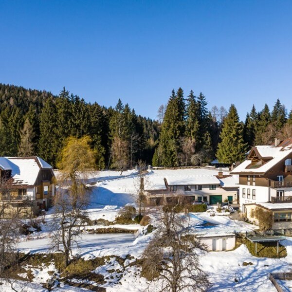 Der Bauernhof mit seinen Gebäuden inmitten einer schneebedeckten Landschaft am Waldrand.