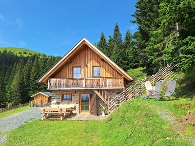 Außenansicht der gemütlichen Alm mit Sonnenterrasse, Gartenmöbeln und Liegestühlen.