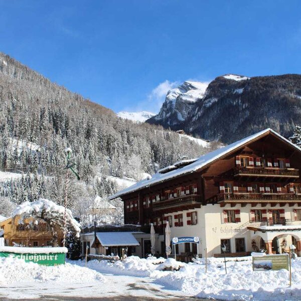 Der Bauernhof mit traditioneller Architektur, verschneitem Dach und Balkonen, umgeben von schneebedeckten Bergen im Winter.