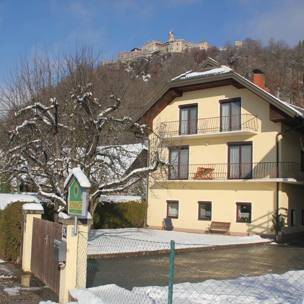 Der Bauernhof SonnHOF mit seinen Ferienwohnungen im Winter, inklusive Balkonen und Blick auf die Burgruine Landskron.