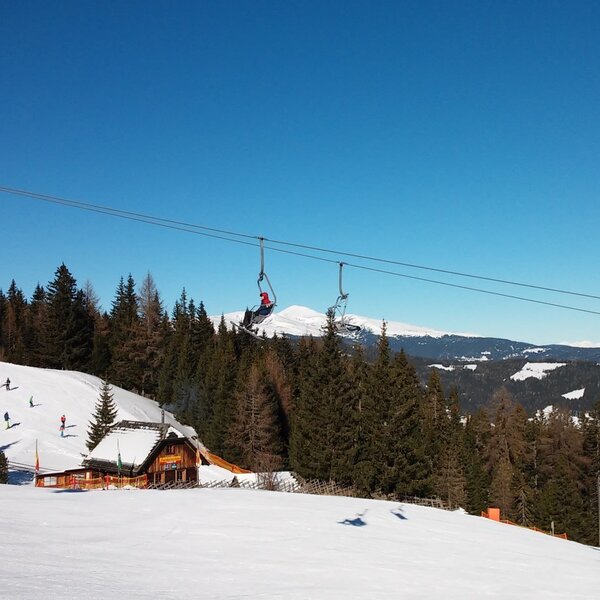 Ski slopes and a chairlift are visible in the alpine landscape surrounding the Alpine Hut, providing access to winter sports.