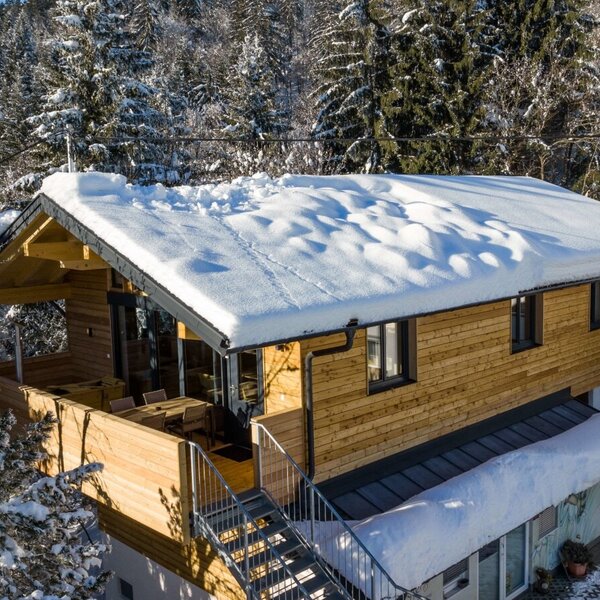 Das Holzgebäude des Bauernhofs mit schneebedecktem Dach, Außentreppe und Balkon mit Sitzgelegenheiten.