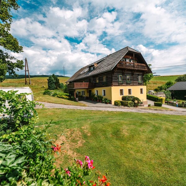 Der renovierte Bauernhof mit Holzbalkonen, umgeben von grünen Rasenflächen und weiteren Hofgebäuden, bietet Platz für Aktivitäten im Freien.