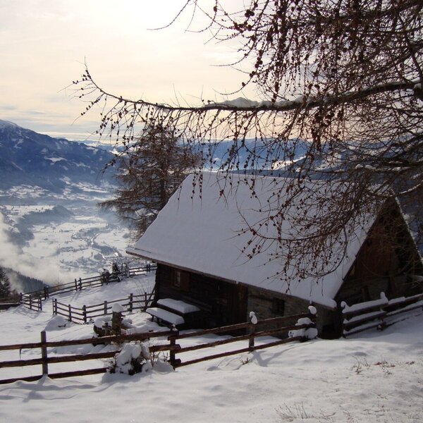 Die verschneite Alm mit traditionellem Holzzaun und Panoramablick auf das winterliche Tal und die Berge.