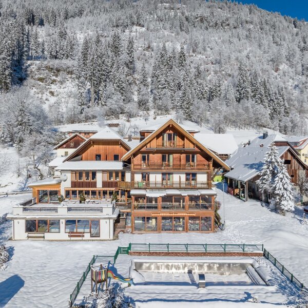 Außenansicht des Bauernhofs im Winter, umgeben von Schnee und Bergen, mit Balkonen und einem Kinderspielbereich.