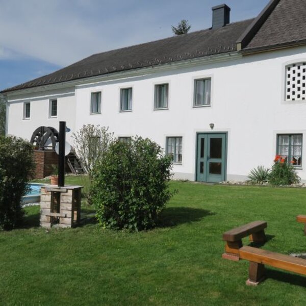 The farm house exterior features a green lawn with wooden benches surrounding a fire pit, a water wheel, and a swimming pool.