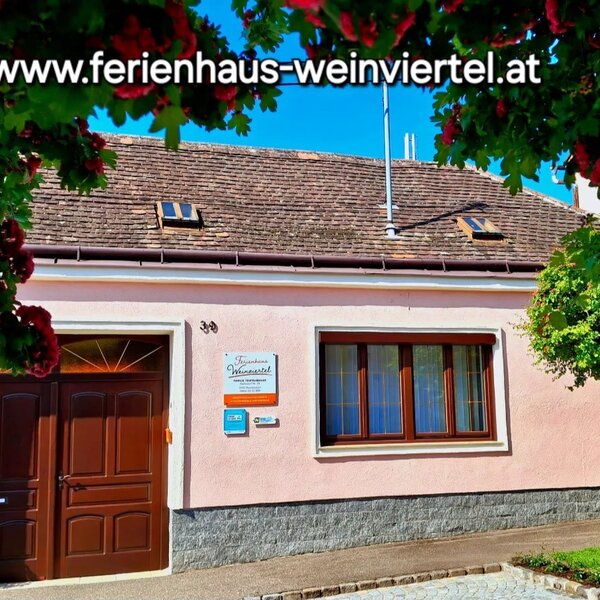 Das Ferienhaus mit heller Fassade, braunen Fenstern und Türen sowie begrünten Bereichen davor.