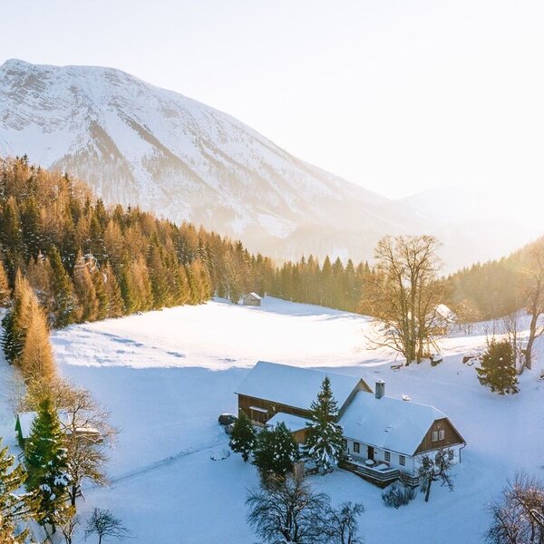 Das Ferienhaus in einer verschneiten Winterlandschaft, umgeben von Wald und Bergen.