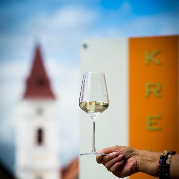 A glass of white wine, with a local church tower and a sign in the background at the farmhouse.