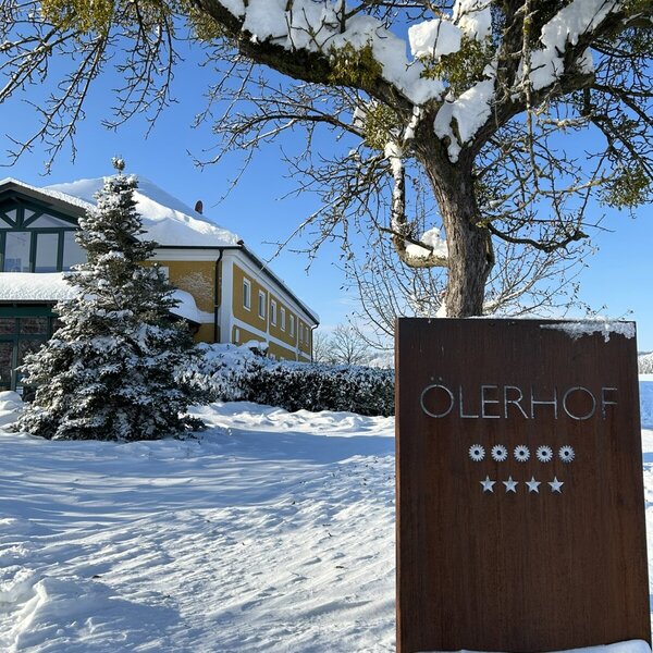 Das Schild des Bauernhofs Ölerhof mit 5 Kreisen und 4 Sternen in verschneiter Winterlandschaft.