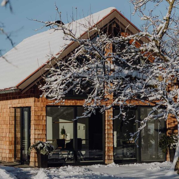 The chalet in the farmhouse's orchard, featuring a wooden shingle facade and large windows, surrounded by snow and trees.