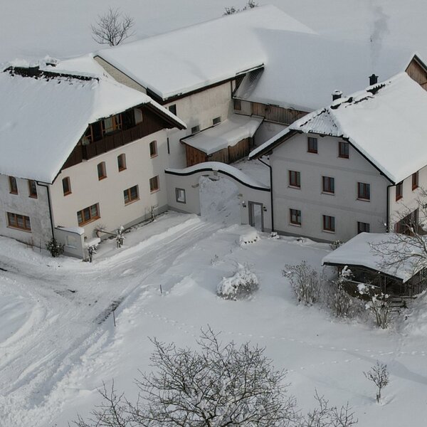 Der Bauernhof im Winter, mit den Gebäuden und der Umgebung schneebedeckt.