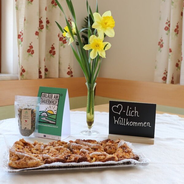 A welcome amenity on a farm house table, featuring pastries, a "Holiday on the Farm" leaflet, a bag of herbs, and fresh daffodils.