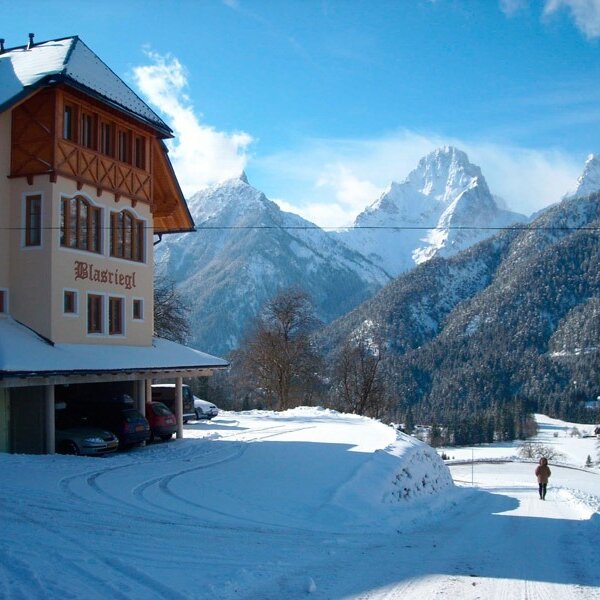 The Farm House "Blasriegl" with an integrated garage, surrounded by snow and snow-capped mountains.