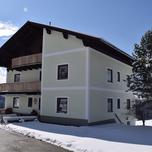 Der Bauernhof mit zwei Balkonen, umgeben von Schnee und Bergen.