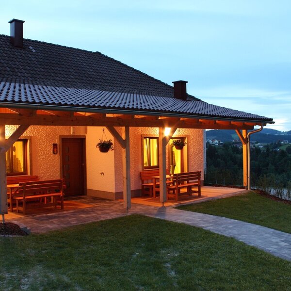 The farm house features a covered terrace with wooden benches and tables, illuminated in the evening, with views of the surrounding hills.