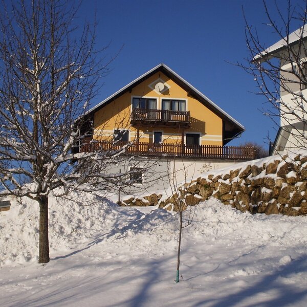 The yellow Farm House in winter, featuring balconies and surrounded by snow-covered trees and a stone wall.
