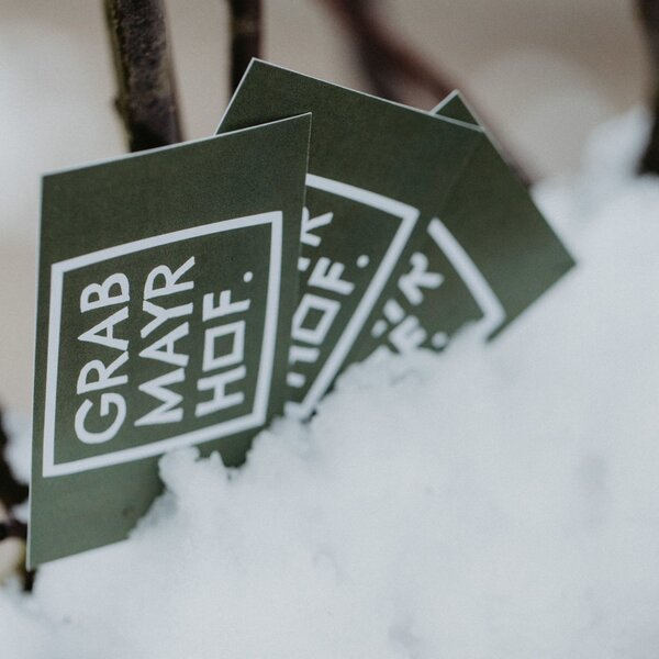 Branding cards for Grab Mayr Hof farm house, partially covered in snow on a tree branch.