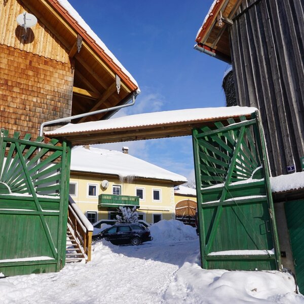 The green entrance gate of the Farm House leads into the snow-covered courtyard, surrounded by traditional buildings.
