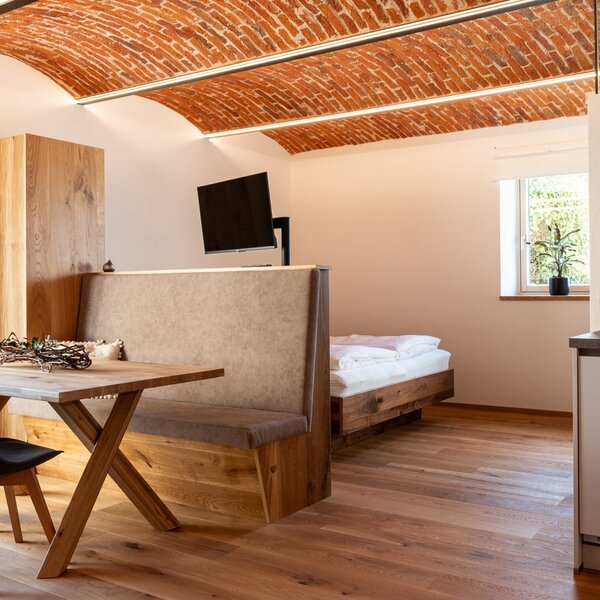 Der kombinierte Wohn- und Schlafbereich des Bauernhofs bietet eine Backstein-Gewölbedecke, einen Esstisch mit Sitzbank, ein Holzbett und eine integrierte Kochnische.