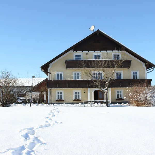 Der Bauernhof von außen im Winter, mit Balkonen und einem verschneiten Kinderspielplatz.