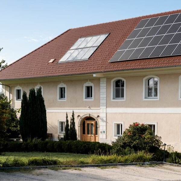 Das einladende Gebäude des Bauernhofs mit einem gepflegten, grünen Garten und modernen Solarmodulen auf dem Dach.