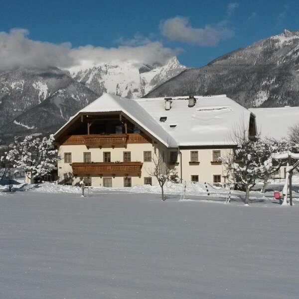 The Farm House exterior in winter, featuring snow-covered roofs, wooden balconies, and a backdrop of snowy mountains.