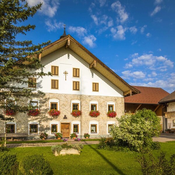 The main Farm House building, featuring a stone and white facade with wooden shutters, flower boxes, and a gabled roof, set amidst a green lawn.