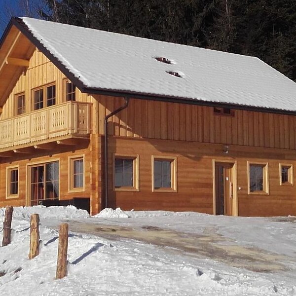 The wooden Farm House features a snow-covered roof and a balcony, set in a snowy landscape with a forest backdrop.