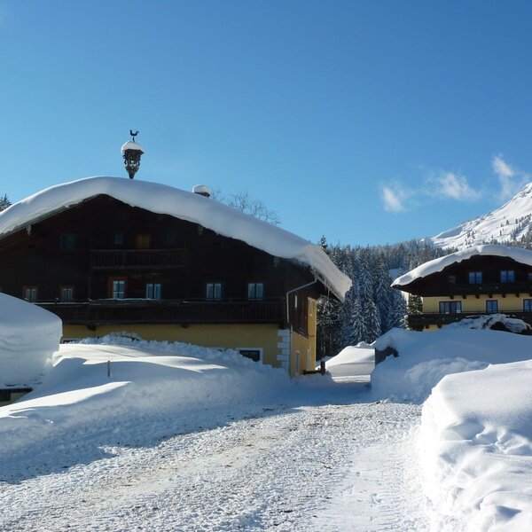 The farmhouse and an adjacent building, seen from the snowy driveway in winter, with snow-covered mountains in the background.