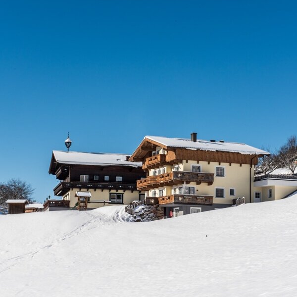 Der Bauernhof im Winter, mit schneebedeckten Dächern und Balkonen in der verschneiten Landschaft.