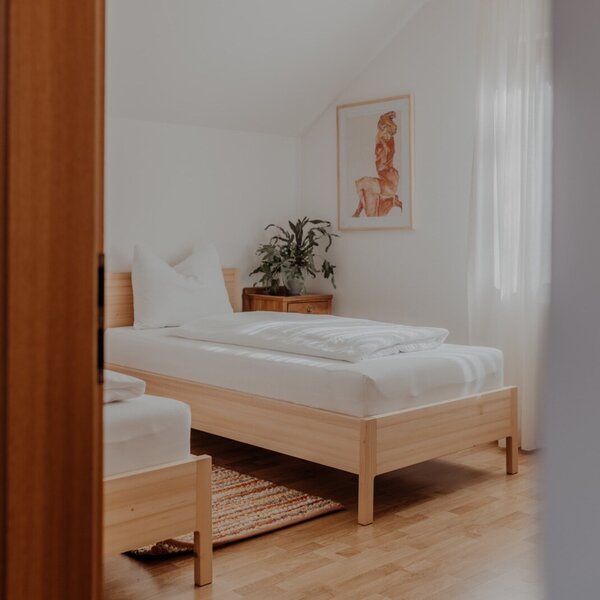 Bedroom in the Farm House with two single wooden-framed beds, white bedding, hardwood floors, a nightstand, and a window with sheer curtains.