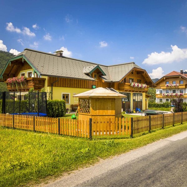 Der Bauernhof mit eingezäuntem Gartenbereich, der ein Trampolin und ein Holzspielhaus umfasst.