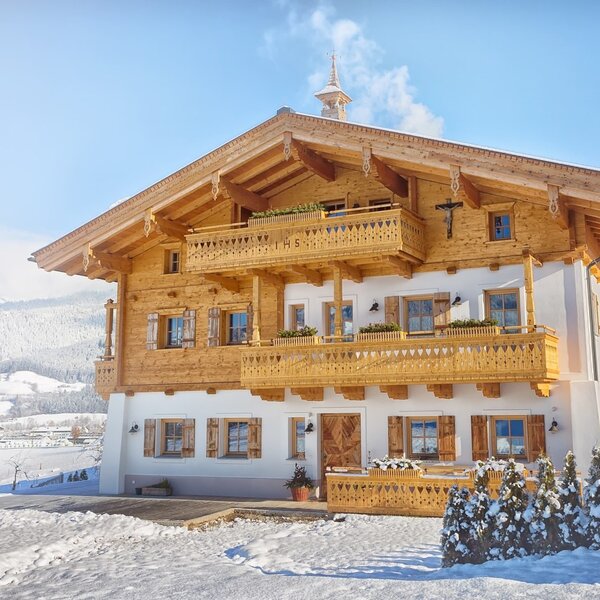 The Farm House exterior in traditional alpine style with wooden balconies and a snow-covered mountain backdrop.