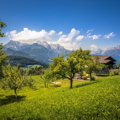 Der Bauernhof mit großem Spielplatz auf grünen Wiesen und Blick auf die umliegenden Berge.