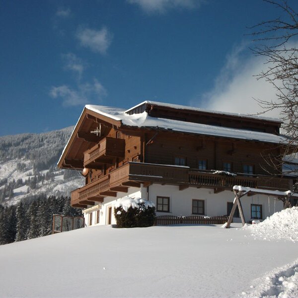 The farmhouse exterior in winter, featuring snow-covered balconies for the holiday apartments and a mountain backdrop.