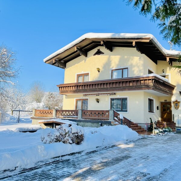 Der schneebedeckte Bauernhof an einem sonnigen Wintertag, mit Balkonen und einer Zufahrt.