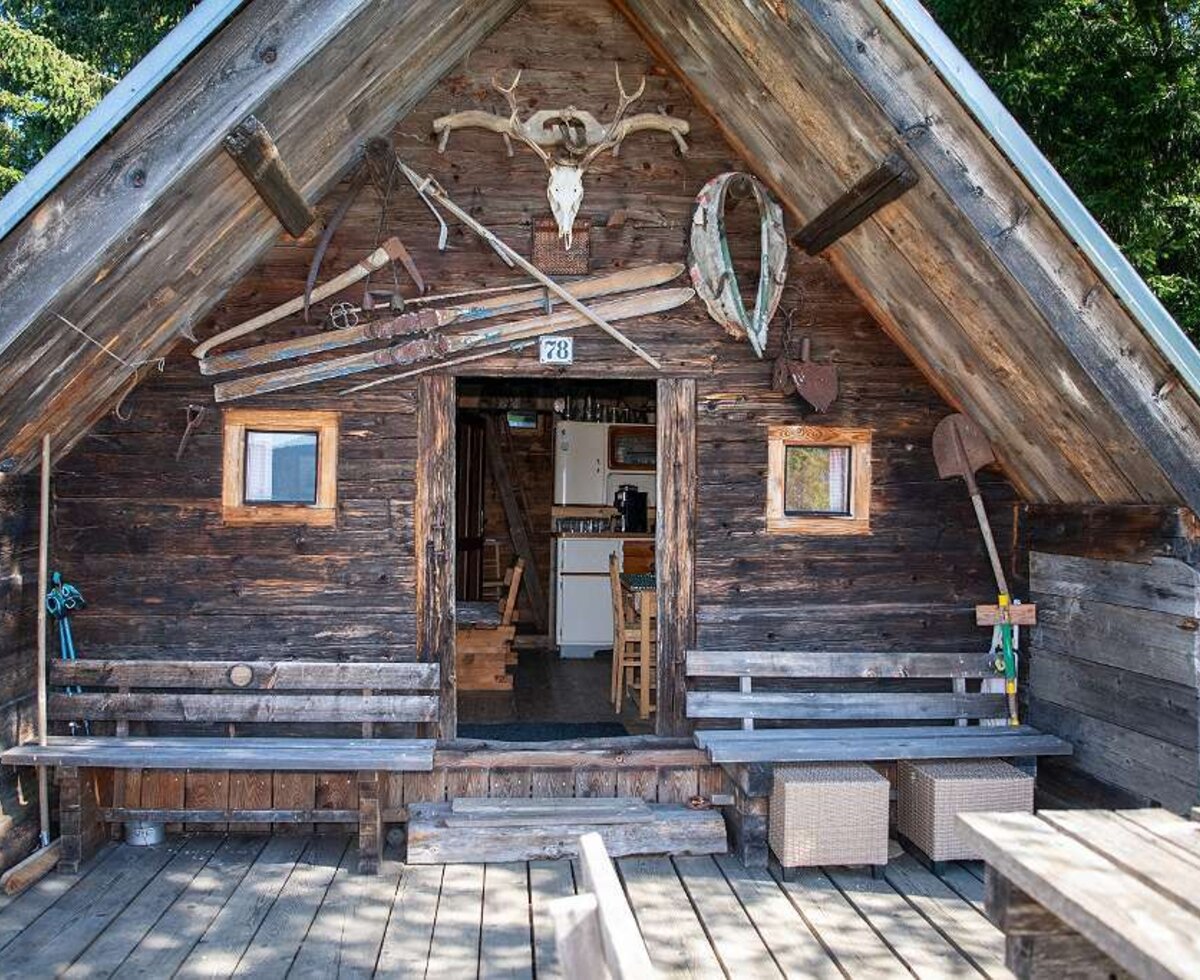 Die Holzfassade des Hofs mit einer Veranda, Sitzbänken und traditionellen Dekorationen wie Geweihen und alten Werkzeugen am Eingang, der einen Blick auf den Küchenbereich bietet.