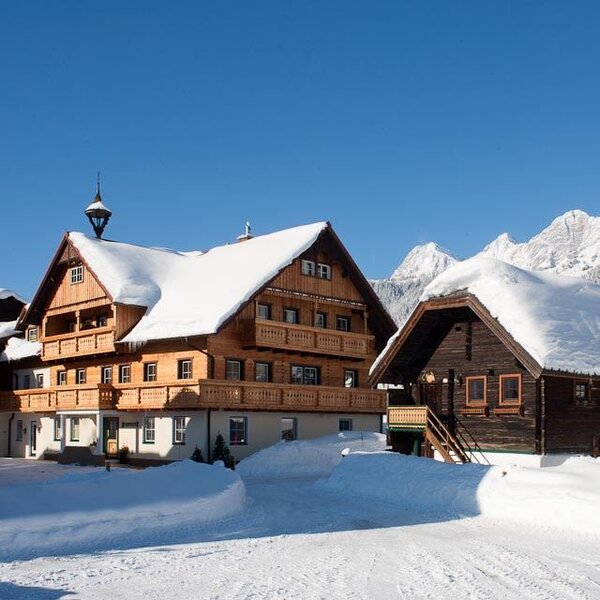 The Farm House and a smaller wooden outbuilding, both covered in snow, with snow-capped mountains visible in the distance.