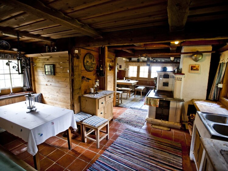 Die Wohnküche der Almhütte verfügt über einen Holzherd mit Kachelofen, fließendes Wasser und zwei Sitzecken.