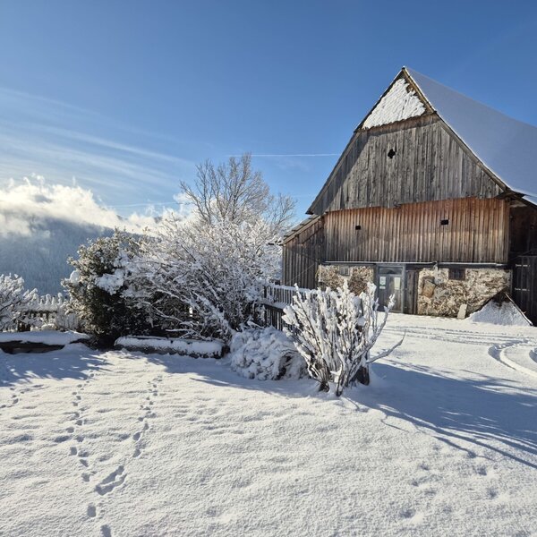 The farmhouse exterior on a clear winter day, surrounded by snow-covered grounds and distant mountain views.