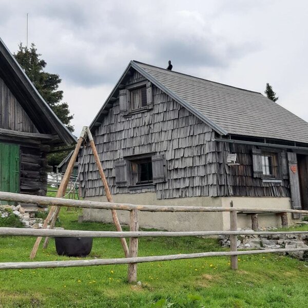Die traditionellen Holzgebäude des Hofes, umgeben von einem Holzzaun und grüner Landschaft.