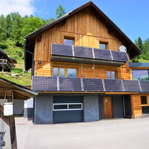 Die Wind Buam Hütte mit einer modernen Holzfassade, Solarmodulen an den Balkonen und umgeben von grüner Natur.