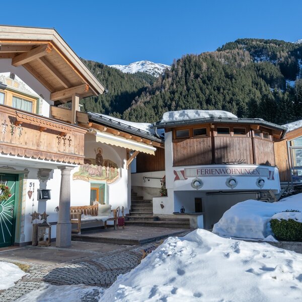 The Farm House exterior, showcasing its holiday apartments and modern glass-fronted section, with snow-covered grounds and a mountain backdrop.