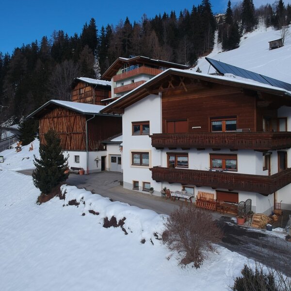 The exterior of the Farm House, featuring wooden balconies, solar panels on the roof, and a snowy mountain setting.