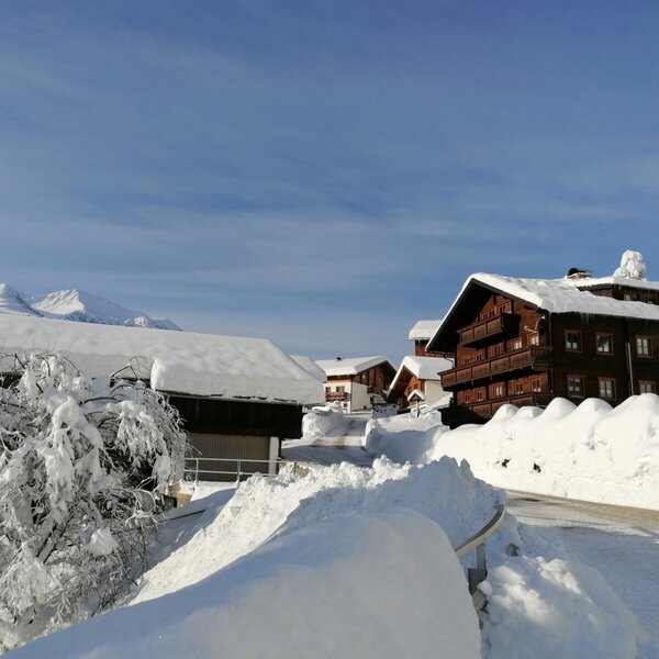 Der Bauernhof in winterlicher Umgebung mit tief verschneiten Gebäuden und Alpenkulisse.
