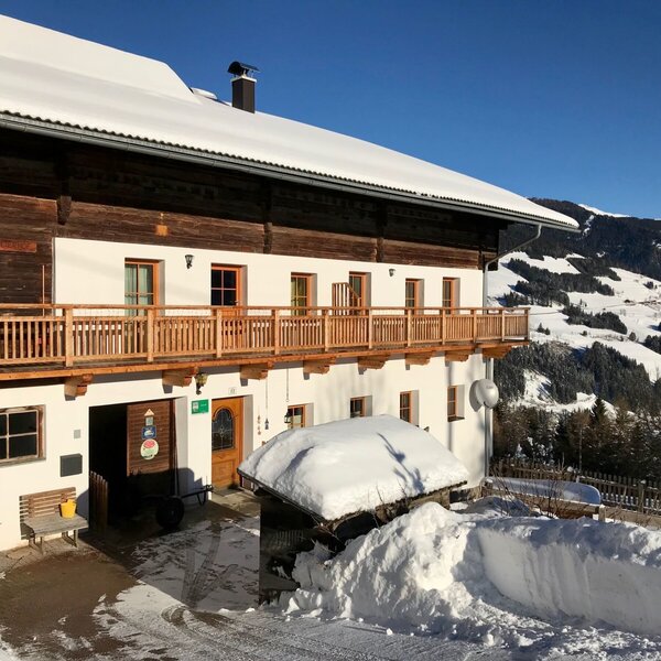 The snow-covered exterior of the Farm House, featuring a wooden balcony and distant snow-capped mountains.
