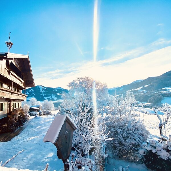 Der Bauernhof im Winter, umgeben von Schnee, mit Panoramablick auf die umliegende Bergwelt.